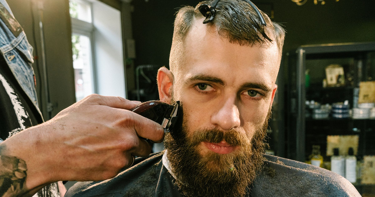 Stylist shaping a full beard with a trimmer during a beard sculpting service